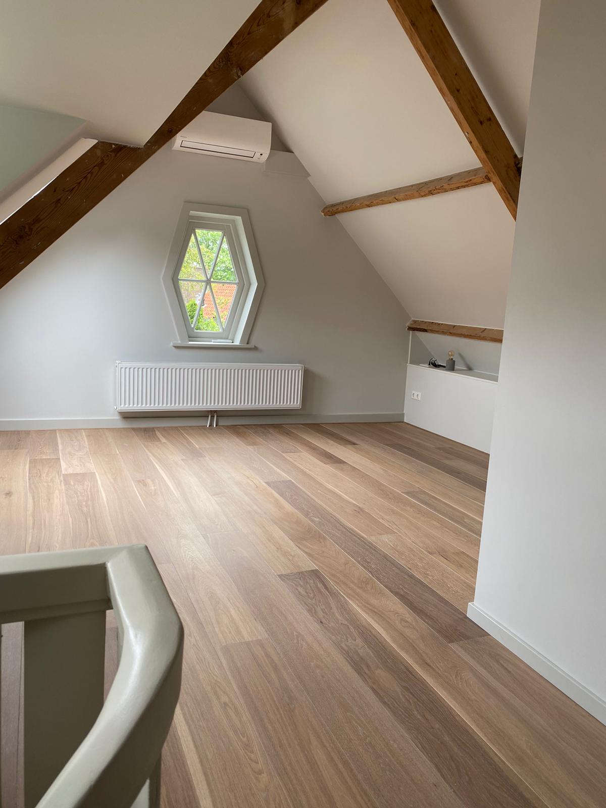 Afgewerkte zolderkamer met houten balken en rond raam