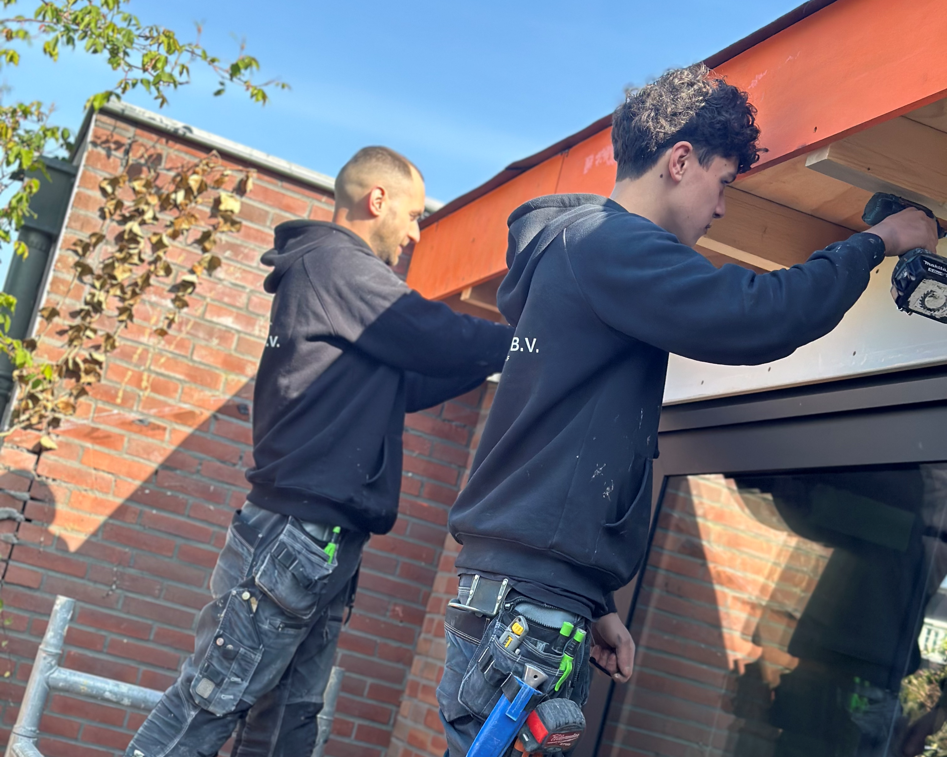 Twee vakmannen die aan een houten dakrand werken.