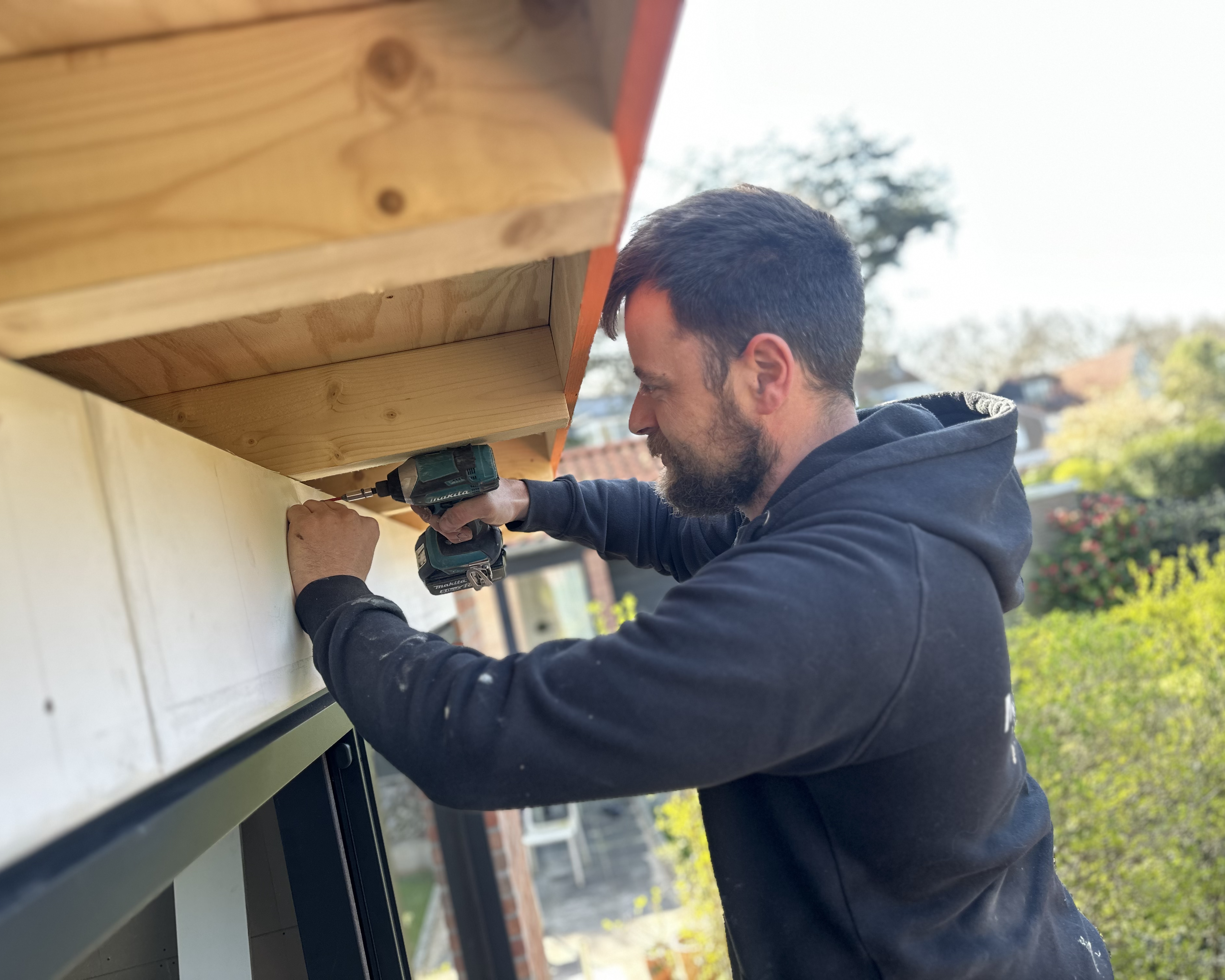 Man die met gereedschap aan een houten dakrand werkt.