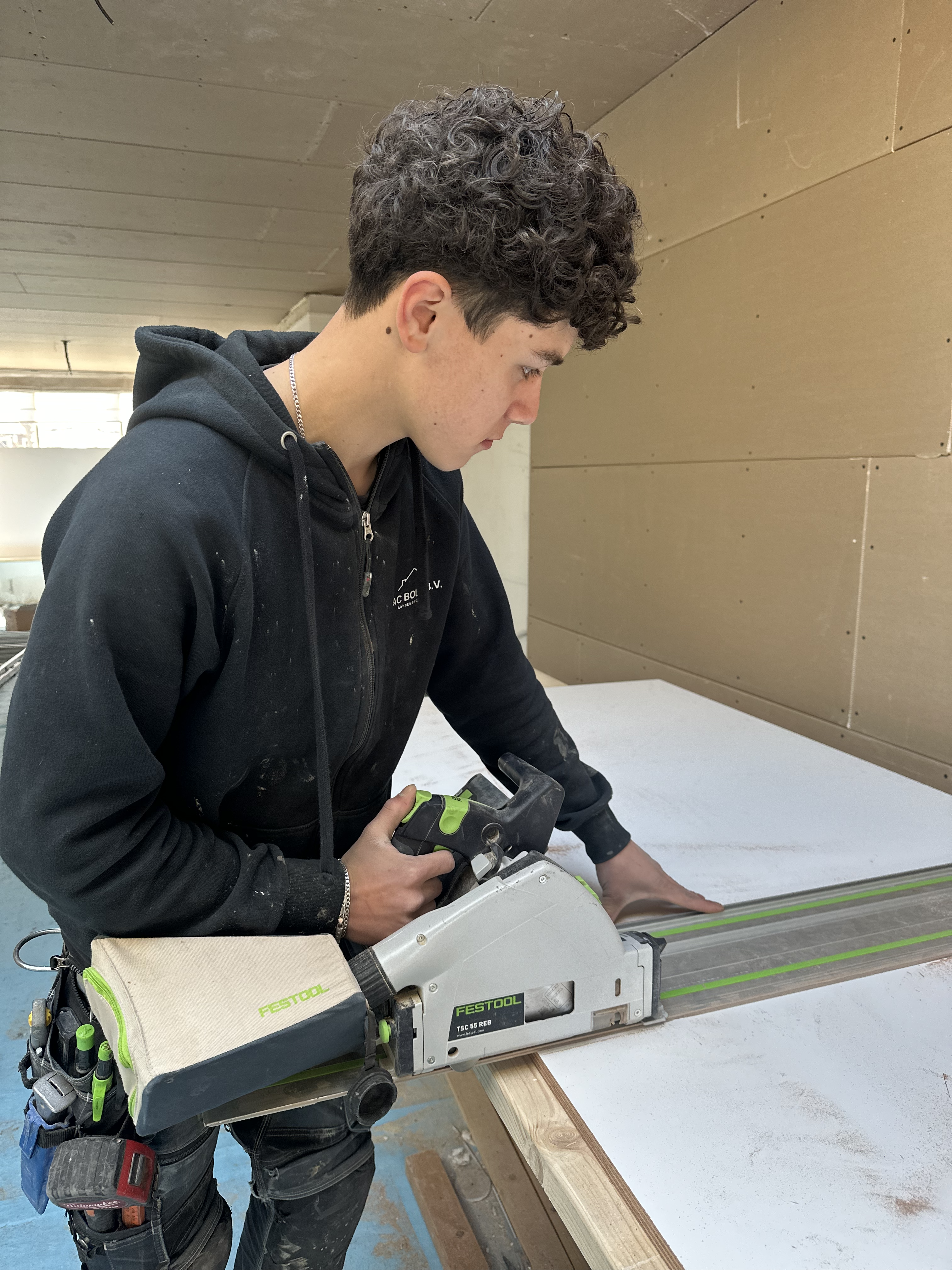 Vakman die met een zaagmachine een houten plaat bewerkt.