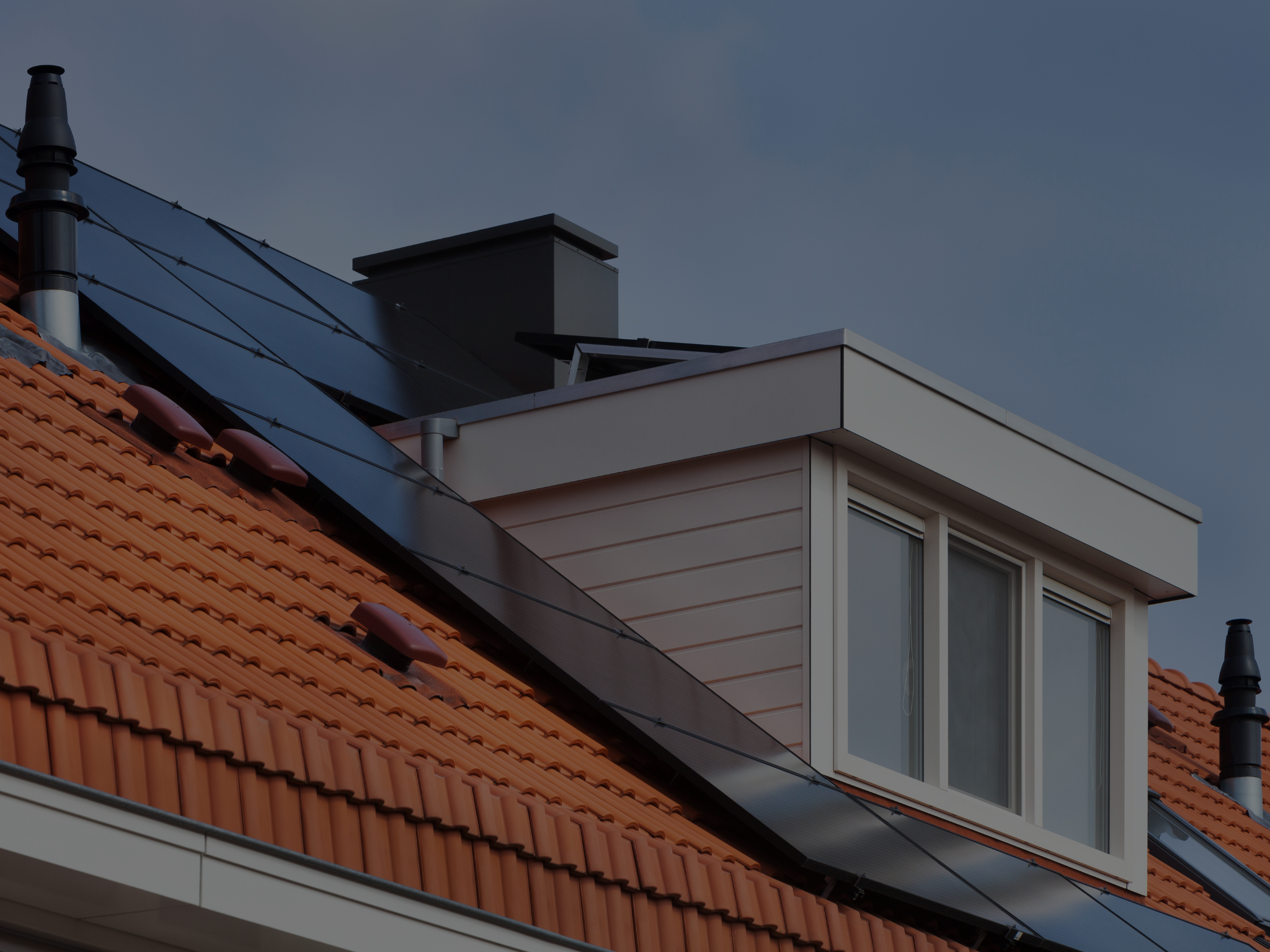 Witte dakkapel op een pannendak naast zonnepanelen.